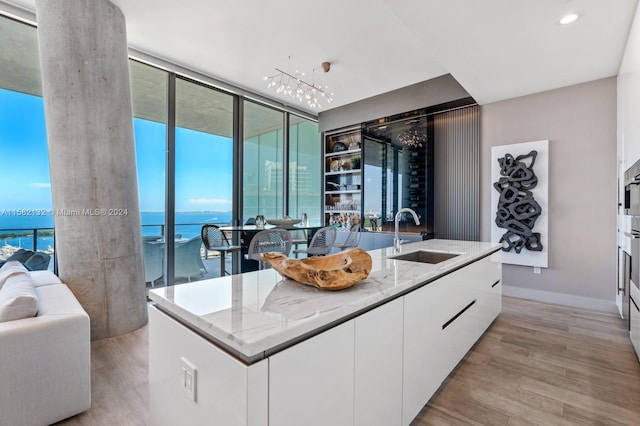 kitchen with white cabinets, a water view, sink, light hardwood / wood-style flooring, and an island with sink