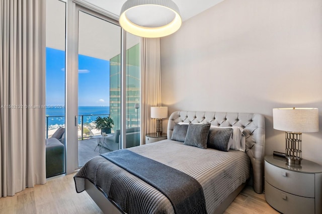 bedroom with access to exterior, a water view, light hardwood / wood-style flooring, and floor to ceiling windows