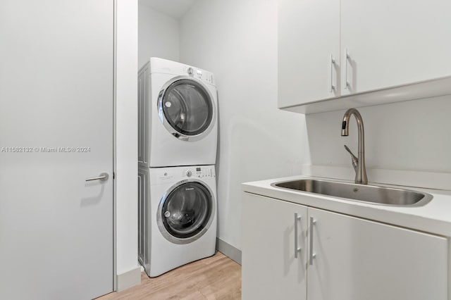 laundry area with stacked washer / dryer, sink, cabinets, and light wood-type flooring