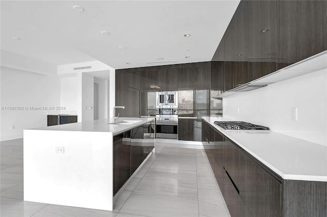 kitchen featuring appliances with stainless steel finishes, sink, light tile floors, and a kitchen island with sink