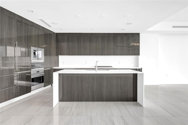 kitchen featuring built in microwave, stainless steel oven, a kitchen island with sink, and light tile floors