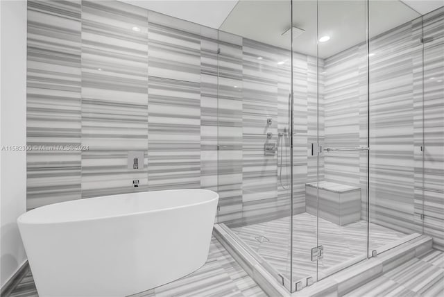 bathroom with shower with separate bathtub and tile walls