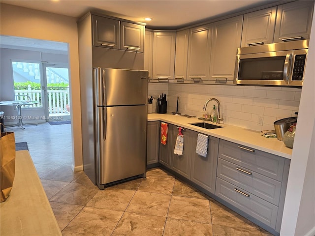 kitchen with gray cabinetry, sink, tasteful backsplash, light tile patterned floors, and appliances with stainless steel finishes