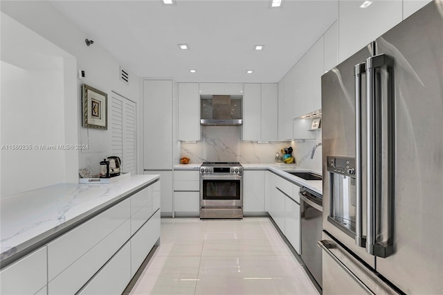 kitchen featuring wall chimney exhaust hood, white cabinetry, appliances with stainless steel finishes, light tile floors, and tasteful backsplash