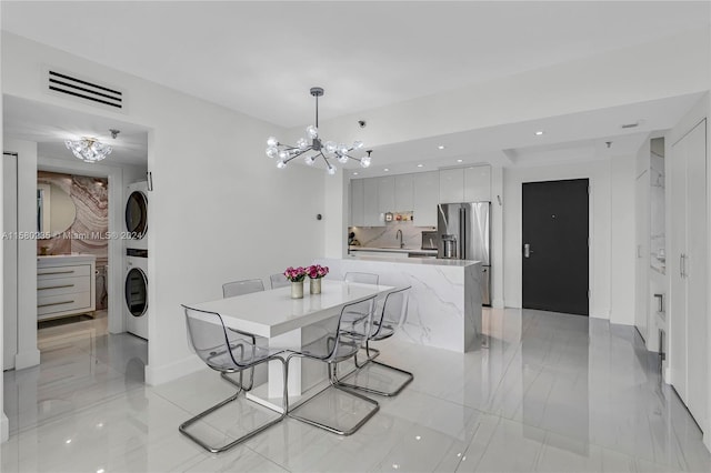 tiled dining room with sink, an inviting chandelier, and stacked washer and dryer