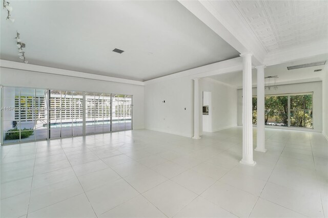 empty room with decorative columns, light tile flooring, and rail lighting