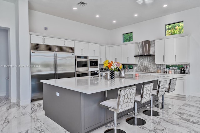 kitchen with appliances with stainless steel finishes, light tile floors, wall chimney range hood, backsplash, and a spacious island