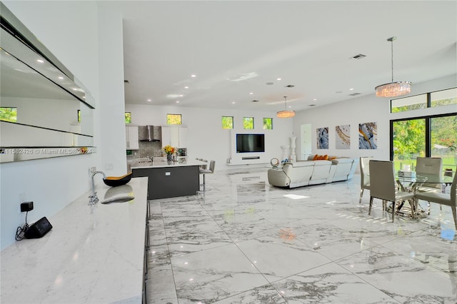 kitchen featuring wall chimney range hood, backsplash, light tile flooring, hanging light fixtures, and plenty of natural light