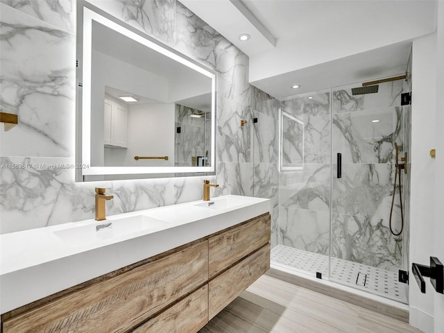 bathroom with dual sinks, tile walls, an enclosed shower, and vanity with extensive cabinet space