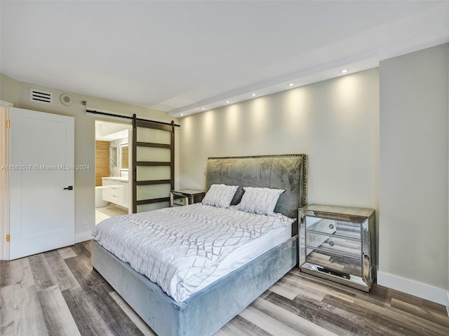 bedroom with ensuite bathroom, wood-type flooring, and a barn door