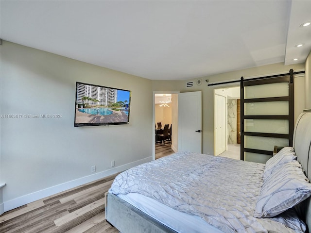 bedroom with a barn door and light hardwood / wood-style flooring