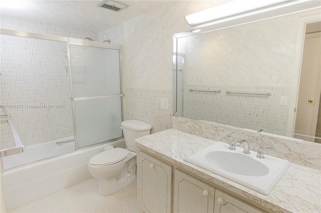 full bathroom featuring tile walls, bath / shower combo with glass door, vanity, tile patterned floors, and toilet