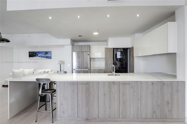 kitchen with a peninsula, light countertops, stacked washer and clothes dryer, modern cabinets, and stainless steel fridge