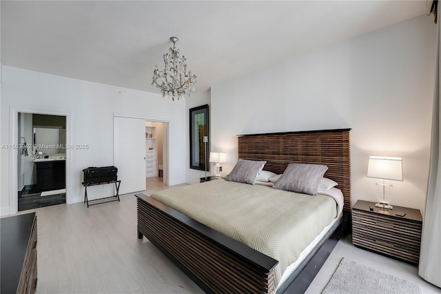 bedroom with a spacious closet, a notable chandelier, ensuite bathroom, and light wood finished floors