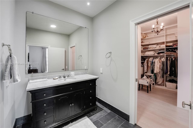 bathroom featuring vanity, a walk in closet, a notable chandelier, and baseboards