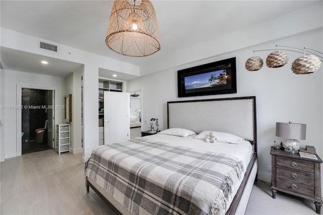 bedroom with light wood-style flooring, visible vents, and connected bathroom