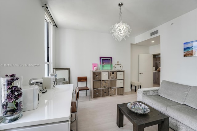 living area featuring visible vents, light wood-style floors, and a chandelier