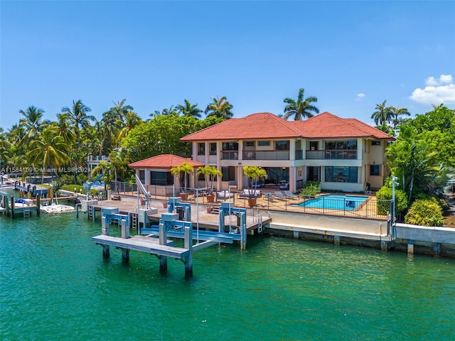 view of dock with a patio area, a swimming pool with hot tub, a balcony, and a water view