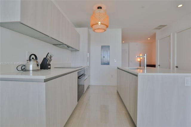 kitchen with sink, wall oven, light wood-type flooring, black electric cooktop, and a center island with sink