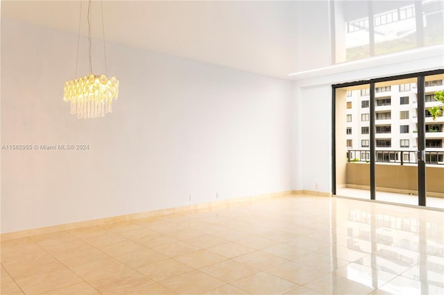 tiled empty room featuring a wealth of natural light and a notable chandelier