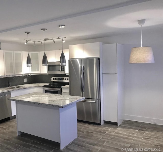 kitchen with a center island, pendant lighting, light stone countertops, stainless steel appliances, and track lighting