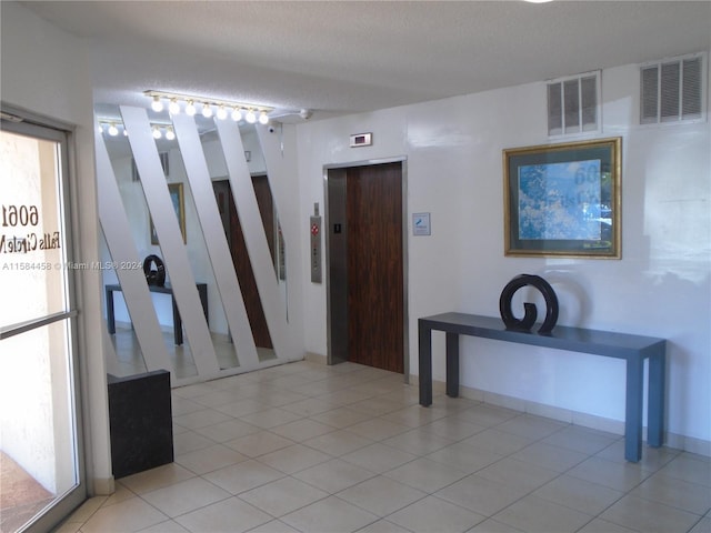 corridor with a textured ceiling, elevator, and light tile patterned flooring