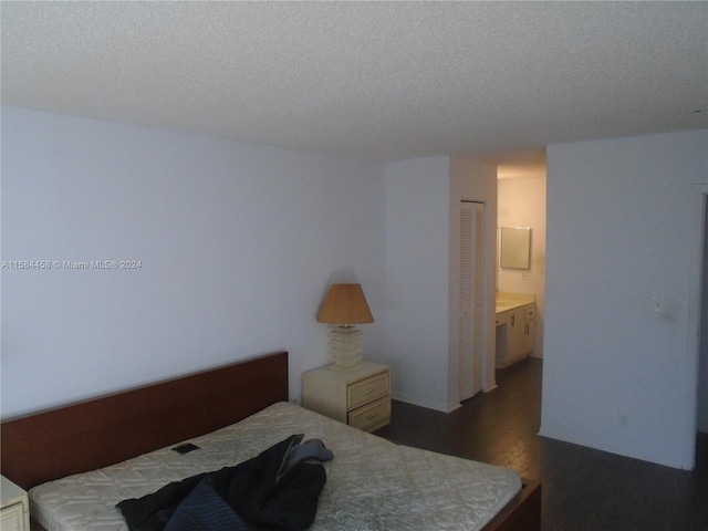 bedroom featuring ensuite bathroom, dark hardwood / wood-style floors, a closet, and a textured ceiling