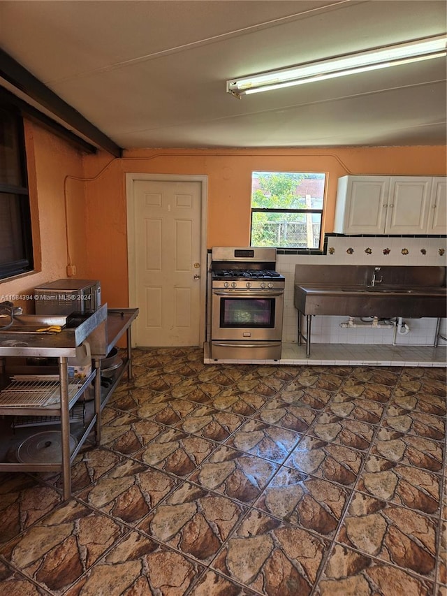 kitchen featuring beamed ceiling, white cabinetry, and stainless steel range with gas stovetop