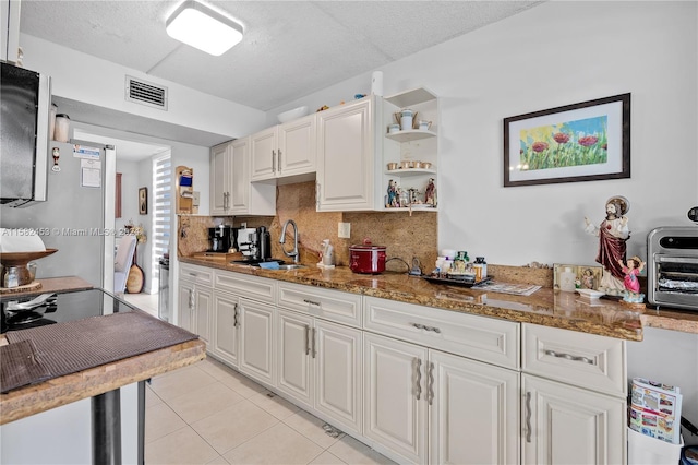 kitchen featuring dark stone countertops, backsplash, white cabinets, and light tile patterned flooring