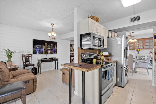 kitchen with a textured ceiling, a notable chandelier, appliances with stainless steel finishes, hanging light fixtures, and white cabinets