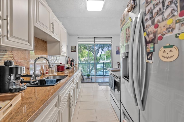 kitchen with white cabinetry, light tile patterned floors, stainless steel appliances, sink, and light stone countertops