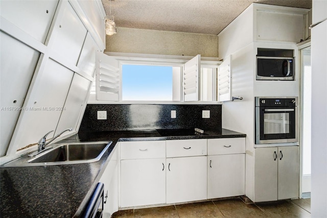 kitchen featuring tasteful backsplash, dark tile flooring, sink, white cabinets, and appliances with stainless steel finishes