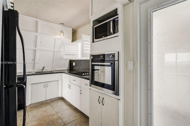 kitchen featuring appliances with stainless steel finishes, white cabinets, backsplash, sink, and light tile floors