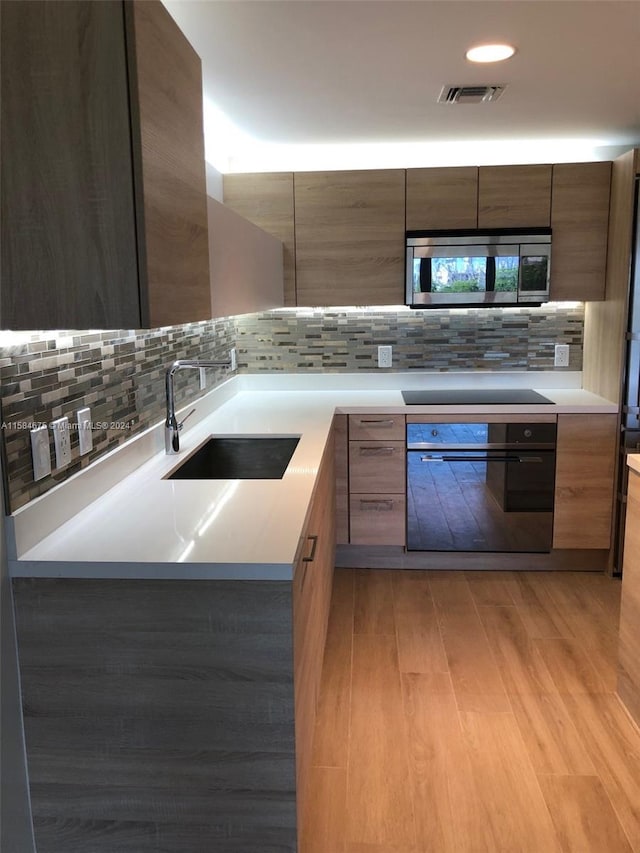 kitchen featuring sink, backsplash, light wood-type flooring, and black appliances