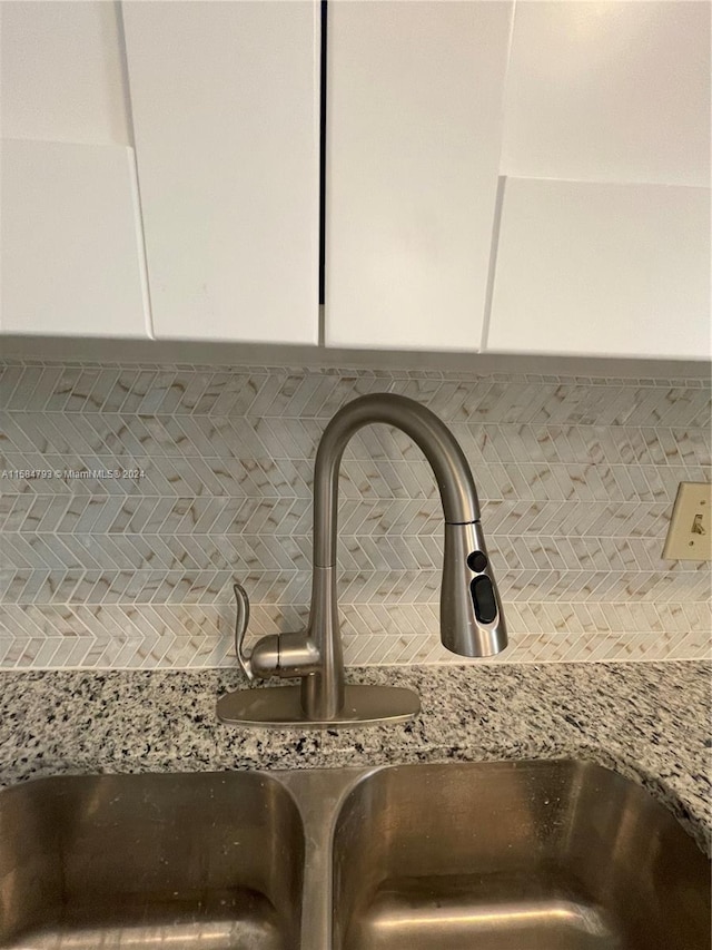 interior details featuring backsplash, light stone countertops, sink, and white cabinets