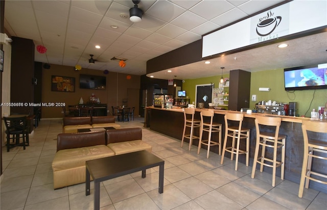 interior space with bar area, ceiling fan, a paneled ceiling, and light tile floors