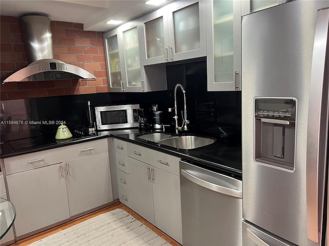 kitchen featuring wall chimney range hood, light hardwood / wood-style floors, stainless steel appliances, sink, and tasteful backsplash