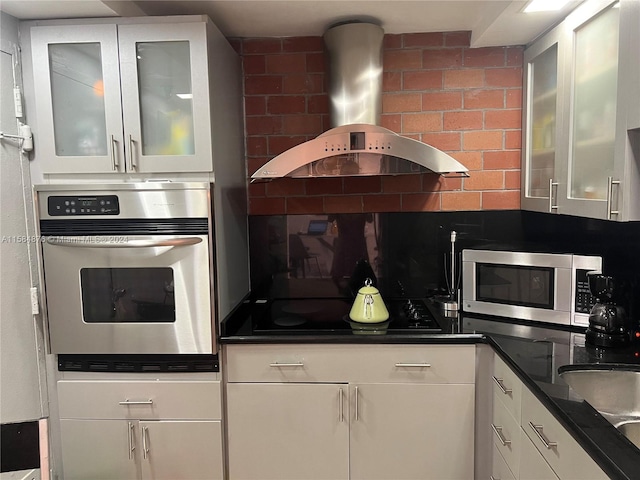 kitchen featuring stainless steel appliances, range hood, backsplash, sink, and white cabinets