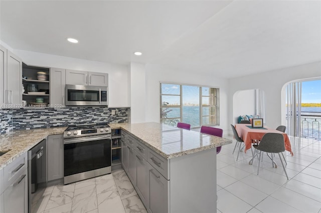 kitchen featuring kitchen peninsula, appliances with stainless steel finishes, gray cabinets, backsplash, and light tile floors