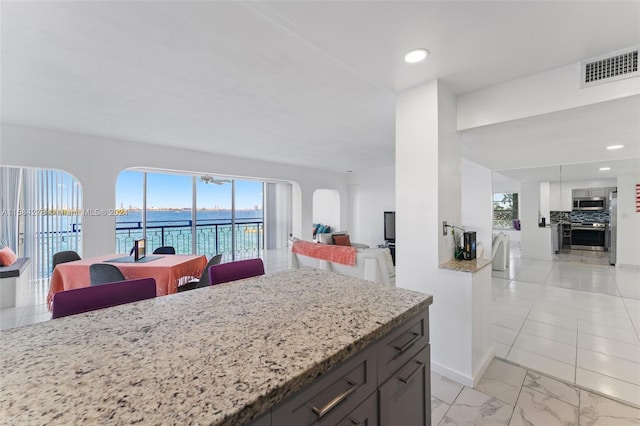 kitchen featuring a water view, tasteful backsplash, stainless steel appliances, and light tile floors