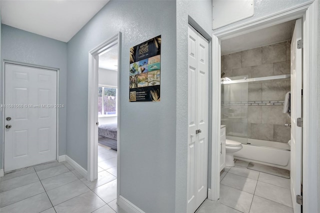 bathroom featuring combined bath / shower with glass door, toilet, and tile flooring