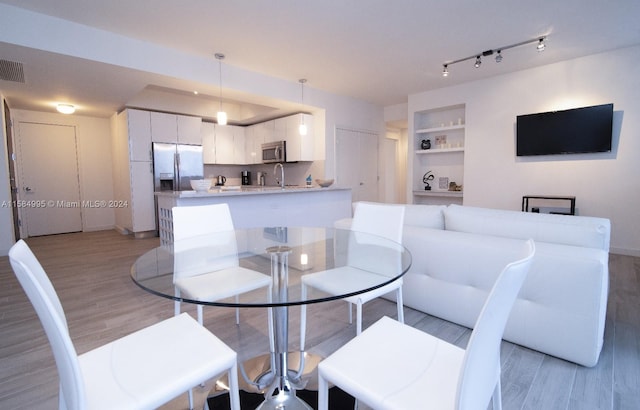 dining space featuring rail lighting, light hardwood / wood-style flooring, built in features, and sink