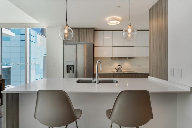 kitchen featuring a kitchen breakfast bar, white cabinets, decorative light fixtures, stainless steel refrigerator with ice dispenser, and sink