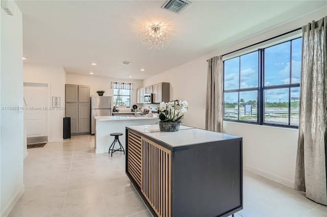 kitchen with a kitchen island, gray cabinets, stainless steel appliances, and light tile flooring