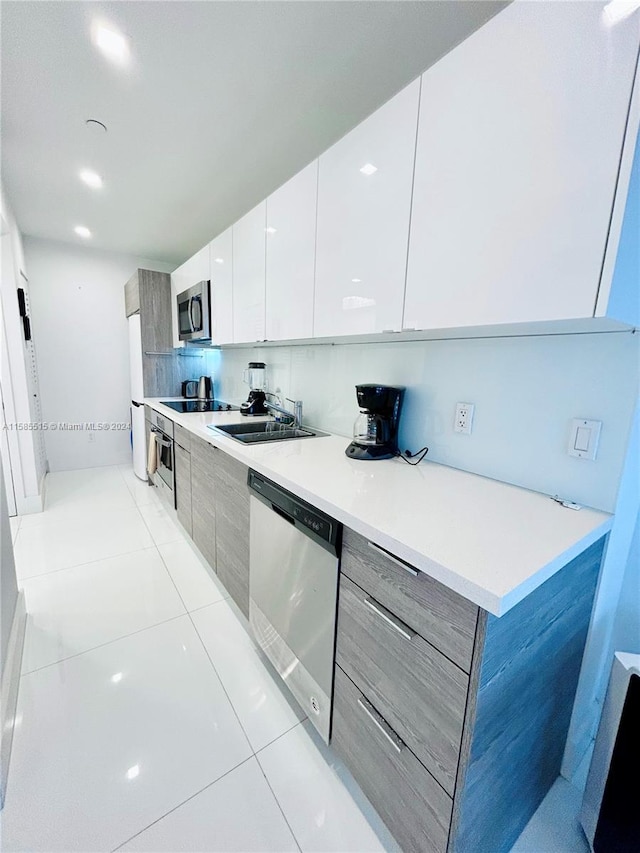 kitchen with stainless steel appliances, backsplash, white cabinetry, sink, and light tile floors