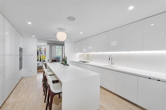 kitchen with a kitchen breakfast bar, light wood-type flooring, sink, white cabinets, and a kitchen island