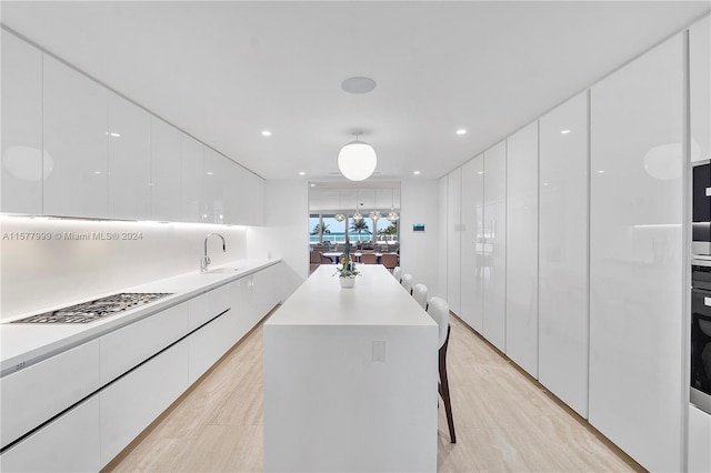 kitchen featuring sink, a kitchen island, a kitchen breakfast bar, light hardwood / wood-style floors, and white cabinets