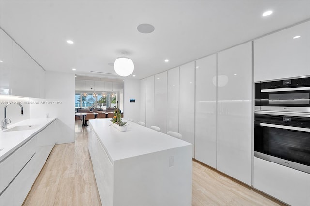 kitchen with sink, a center island, double oven, white cabinets, and light wood-type flooring