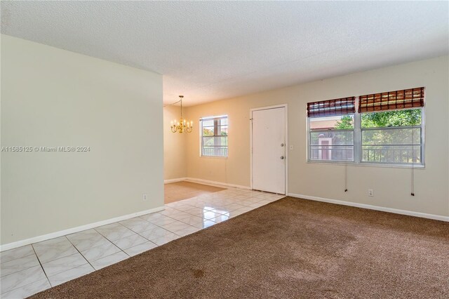 carpeted empty room featuring an inviting chandelier and a textured ceiling