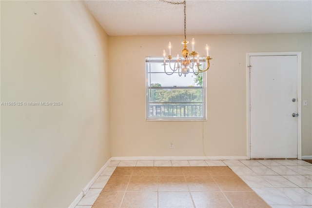 empty room featuring a textured ceiling, light tile flooring, and a chandelier